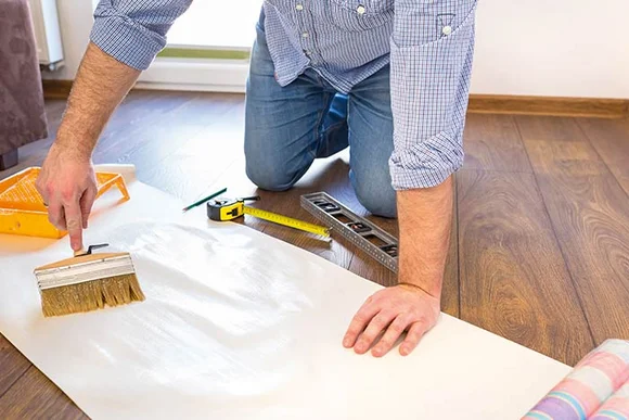 Person trägt Kleister mit Pinsel auf Tapete auf